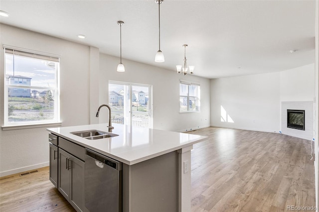 kitchen with pendant lighting, dishwasher, sink, a kitchen island with sink, and light wood-type flooring