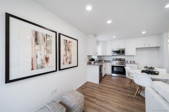 kitchen with wood-type flooring, stainless steel appliances, dark stone counters, and white cabinets