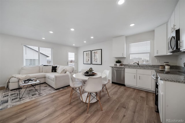 kitchen with sink, light stone counters, appliances with stainless steel finishes, light hardwood / wood-style floors, and white cabinets