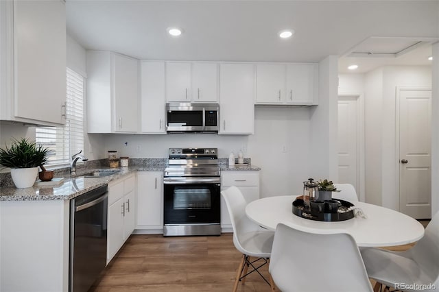 kitchen with stainless steel appliances, white cabinetry, light stone countertops, and sink