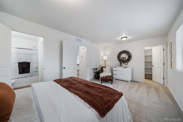 bedroom with ensuite bathroom, a spacious closet, and light colored carpet