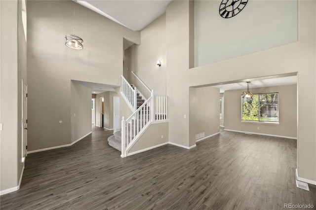 unfurnished living room featuring a high ceiling, dark wood finished floors, baseboards, and stairway