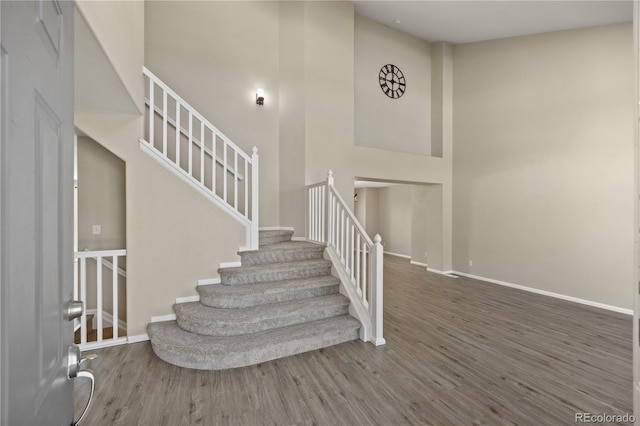 stairway featuring baseboards, wood finished floors, and a towering ceiling