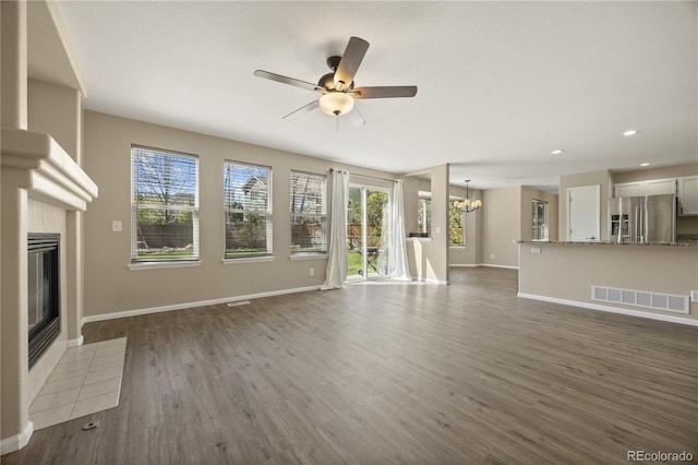 unfurnished living room featuring visible vents, a tiled fireplace, ceiling fan with notable chandelier, and plenty of natural light