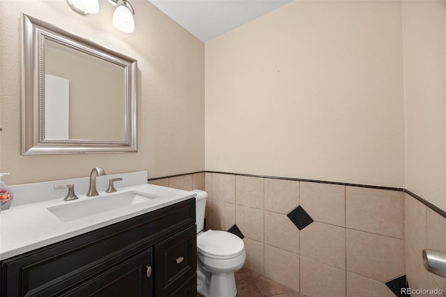 half bathroom with wainscoting, tile patterned flooring, vanity, toilet, and tile walls