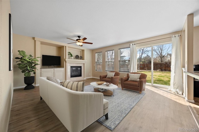 living room with a ceiling fan, a tiled fireplace, a wealth of natural light, and wood finished floors