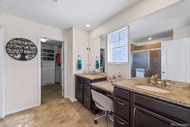 full bath with a stall shower, a spacious closet, two vanities, and a sink