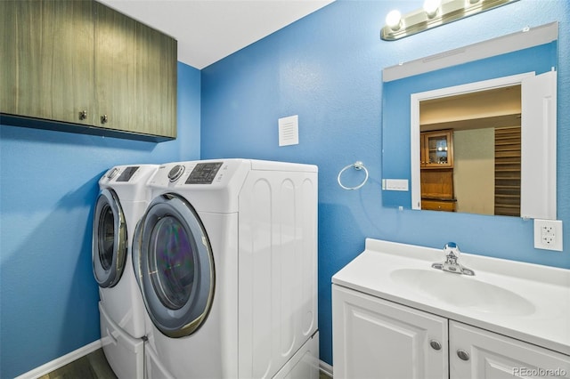 clothes washing area featuring a sink, washing machine and dryer, and cabinet space