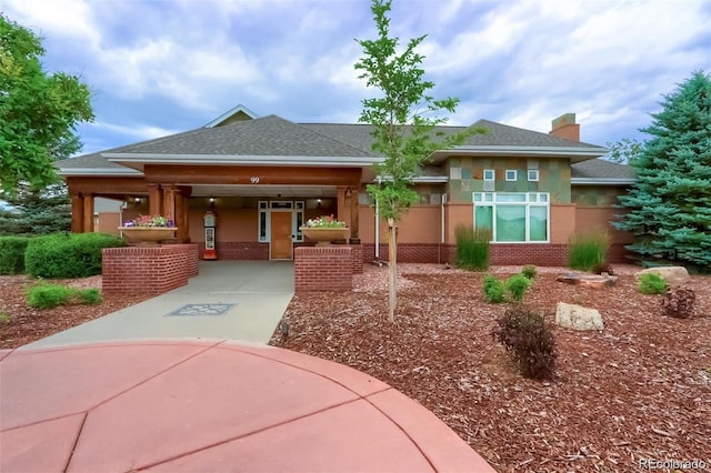 view of front of home with stucco siding, brick siding, a chimney, and roof with shingles