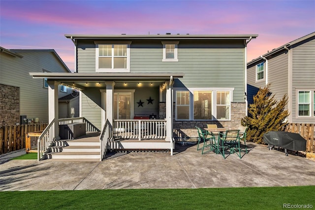 back of property at dusk with a patio, stone siding, and fence