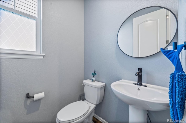 half bath featuring a textured wall, baseboards, a sink, and toilet