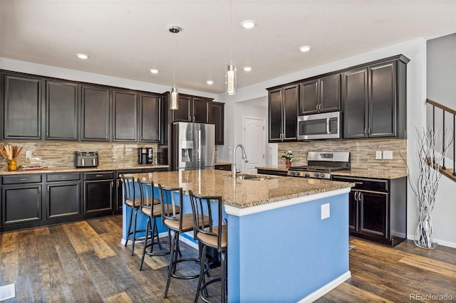 kitchen featuring a breakfast bar area, stainless steel appliances, dark wood-type flooring, a sink, and light stone countertops