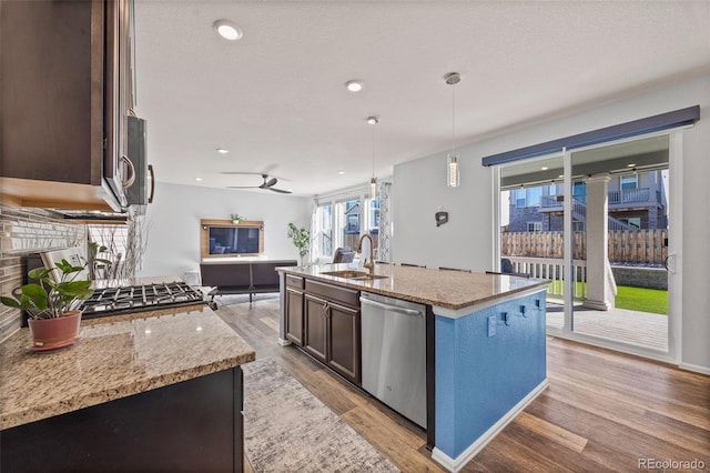 kitchen with light stone countertops, light wood-type flooring, stainless steel dishwasher, a fireplace, and a sink