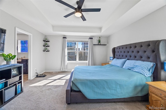 bedroom featuring baseboards, a ceiling fan, ensuite bathroom, a tray ceiling, and carpet flooring