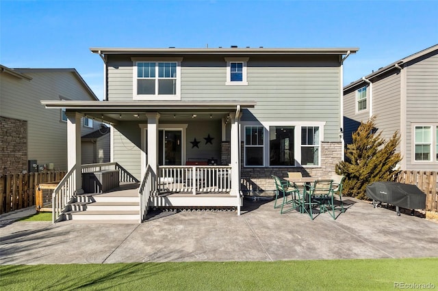 rear view of property featuring a patio, stone siding, and fence