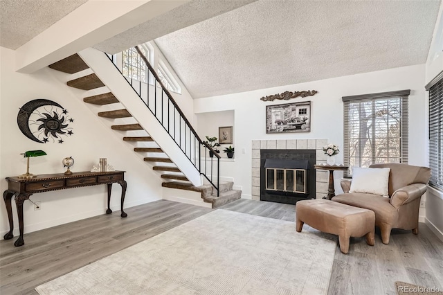 interior space featuring lofted ceiling, a tiled fireplace, wood finished floors, and stairs