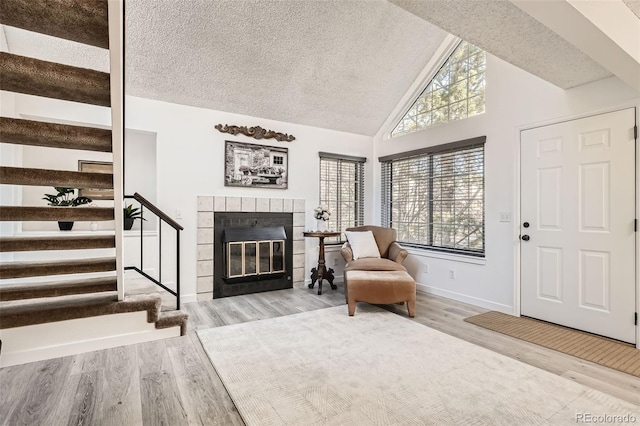 sitting room with a textured ceiling, stairway, a tiled fireplace, and wood finished floors