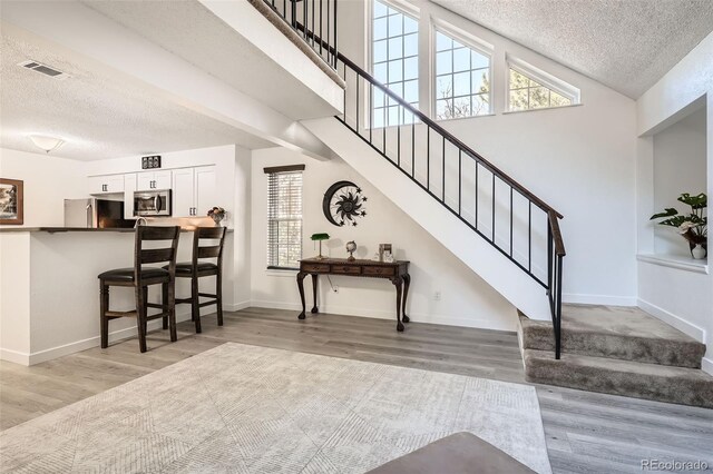 entrance foyer featuring visible vents, a textured ceiling, baseboards, and wood finished floors