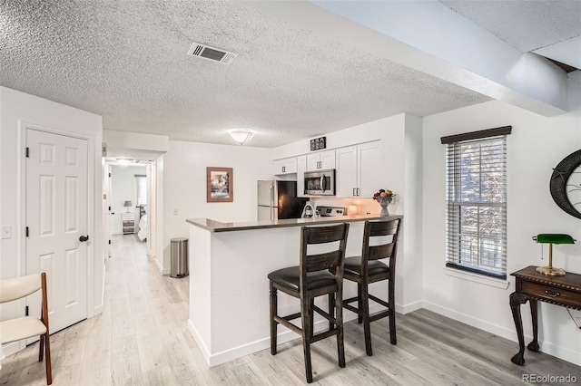 kitchen featuring light wood-style flooring, stainless steel appliances, a peninsula, a breakfast bar, and visible vents