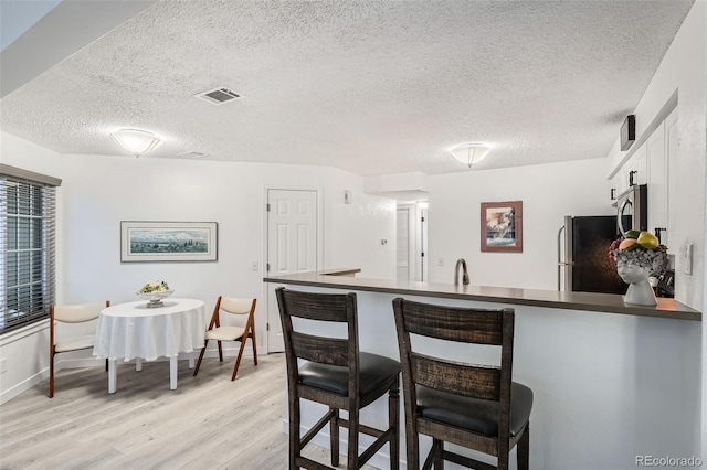 kitchen featuring visible vents, dark countertops, a breakfast bar area, freestanding refrigerator, and a peninsula