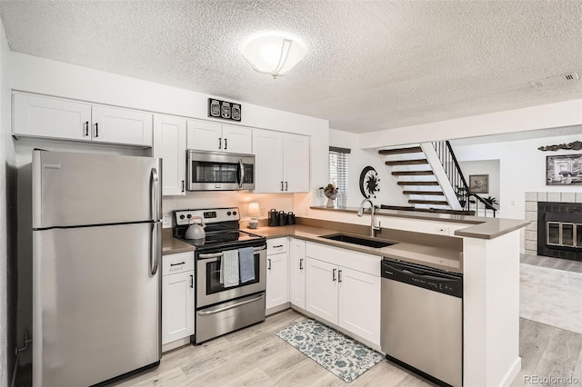 kitchen with appliances with stainless steel finishes, a sink, light wood-type flooring, a tile fireplace, and a peninsula