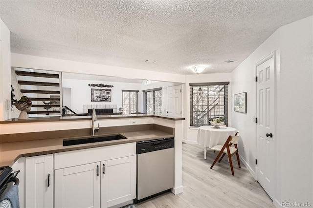 kitchen featuring a sink, white cabinets, stainless steel dishwasher, light wood-type flooring, and dark countertops