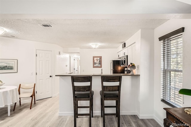 kitchen with a peninsula, stainless steel microwave, a breakfast bar area, and light wood-style flooring