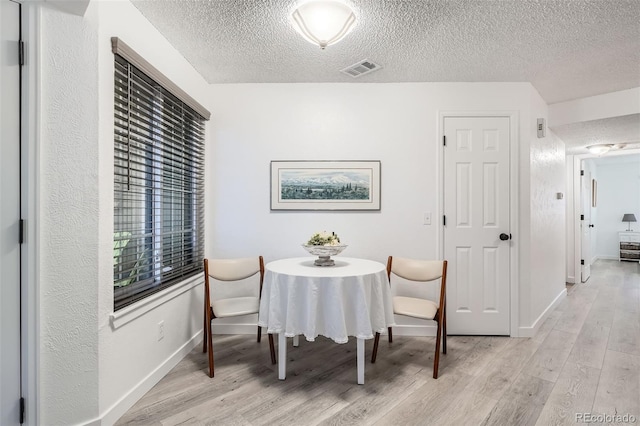 dining room with a textured ceiling, light wood-type flooring, visible vents, and baseboards