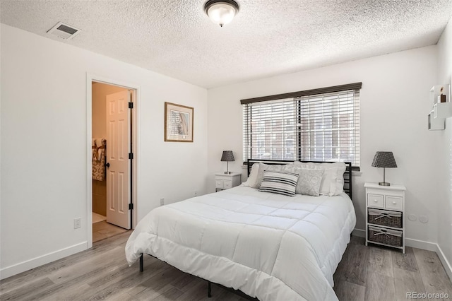 bedroom featuring light wood finished floors, baseboards, visible vents, and a textured ceiling