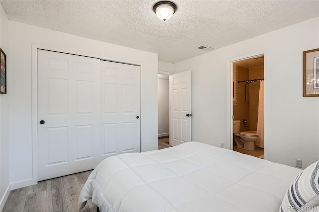 bedroom featuring visible vents, wood finished floors, ensuite bathroom, a textured ceiling, and a closet