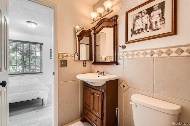 bathroom with toilet, a wainscoted wall, a textured ceiling, vanity, and tile walls