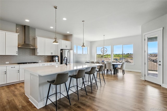 18212 W 95th Pl, Arvada, CO 80007 - kitchen featuring wall chimney range hood, freestanding refrigerator, black stovetop, a large island, and wood finished floors