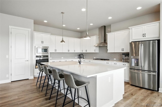 18212 W 95th Pl, Arvada, CO 80007 - kitchen featuring appliances with stainless steel finishes, wall chimney range hood, a spacious island, light wood finished floors, and recessed lighting