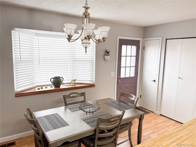 dining space featuring an inviting chandelier, a textured ceiling, and light wood-type flooring