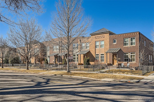 townhome / multi-family property with a residential view, a standing seam roof, brick siding, and fence