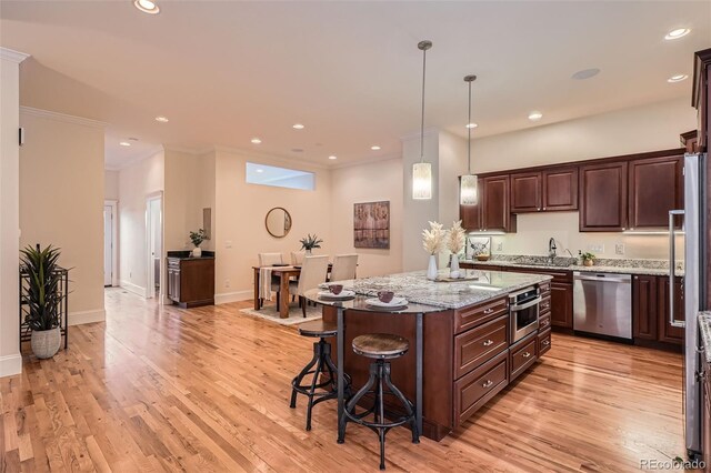 kitchen with stainless steel appliances, a sink, a kitchen island, light wood-type flooring, and a kitchen bar