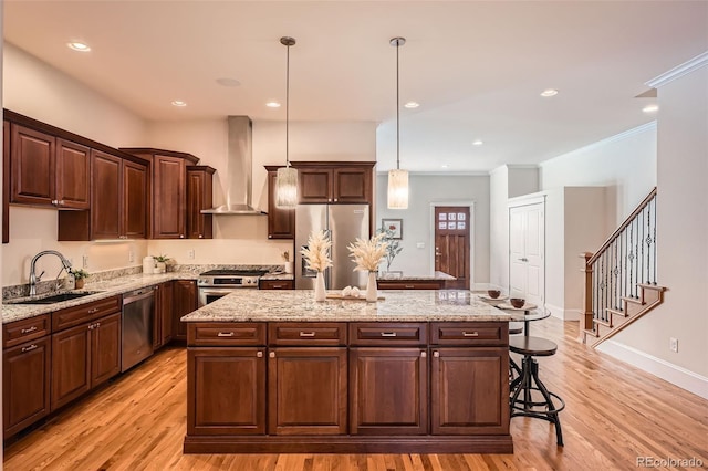 kitchen with stainless steel appliances, light wood-style flooring, a sink, a kitchen island, and wall chimney exhaust hood