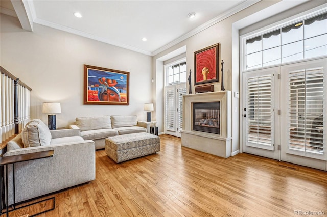 living area featuring visible vents, a glass covered fireplace, light wood-style flooring, crown molding, and recessed lighting