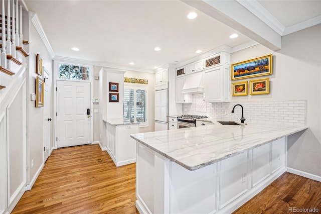 kitchen featuring a sink, a peninsula, stainless steel range with gas stovetop, and premium range hood