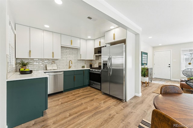 kitchen featuring light wood finished floors, green cabinets, light countertops, decorative backsplash, and appliances with stainless steel finishes