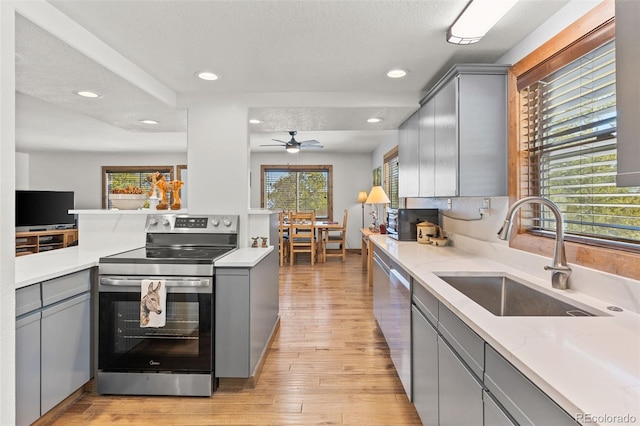 kitchen with stainless steel appliances, light wood-style flooring, gray cabinetry, a sink, and a textured ceiling