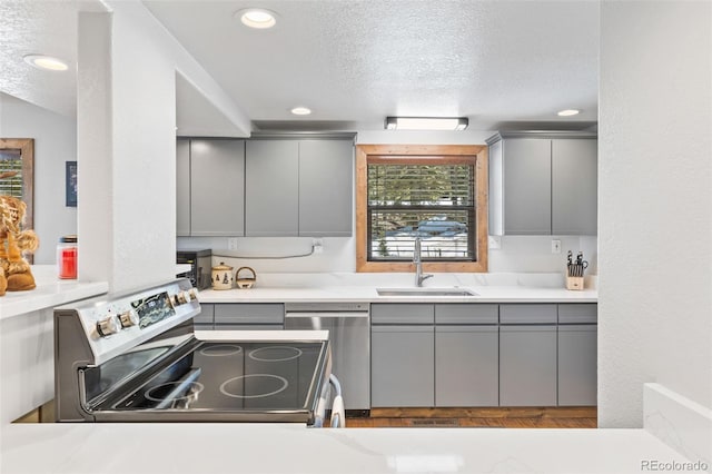 kitchen with a textured ceiling, stainless steel appliances, a sink, and gray cabinetry