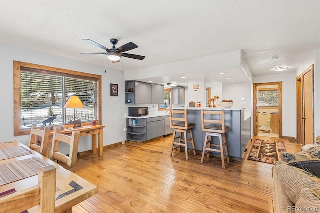 living room featuring baseboards, a ceiling fan, a textured ceiling, light wood-style floors, and recessed lighting