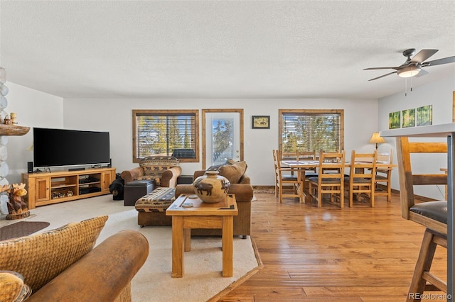 living area with light wood-style flooring, ceiling fan, and a textured ceiling