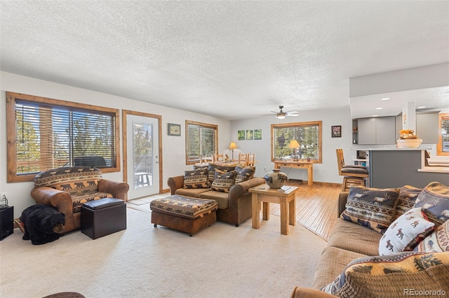 living area with a textured ceiling, ceiling fan, and light colored carpet