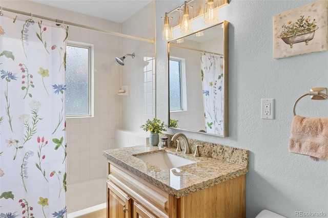 bathroom with a textured wall, vanity, and shower / bathtub combination with curtain