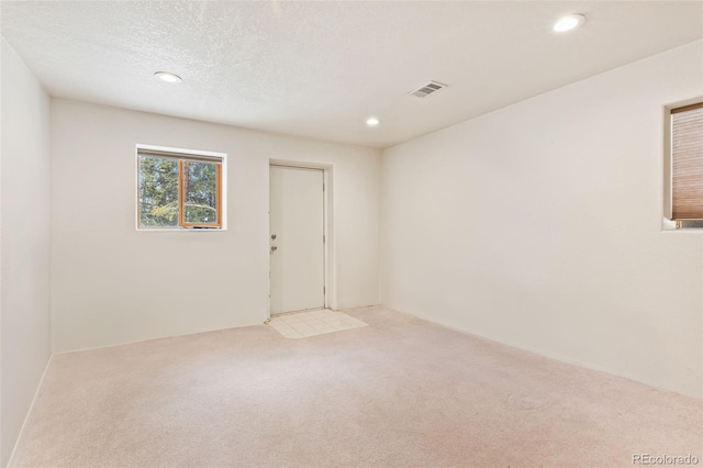 carpeted empty room with visible vents, a textured ceiling, and recessed lighting