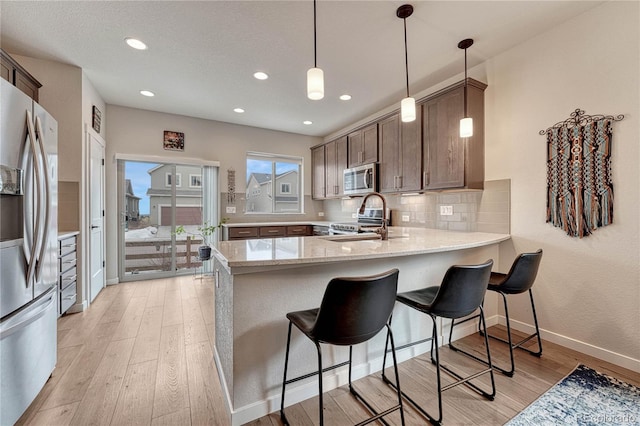 692 Sage Forest Ln, Monument, CO 80132 - kitchen featuring appliances with stainless steel finishes, a peninsula, a sink, light wood-style flooring, and baseboards