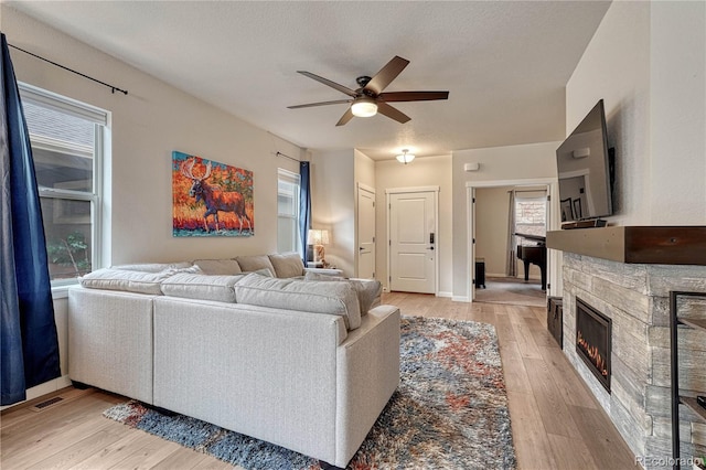 692 Sage Forest Ln, Monument, CO 80132 - living room featuring ceiling fan, light wood finished floors, a stone fireplace, and baseboards