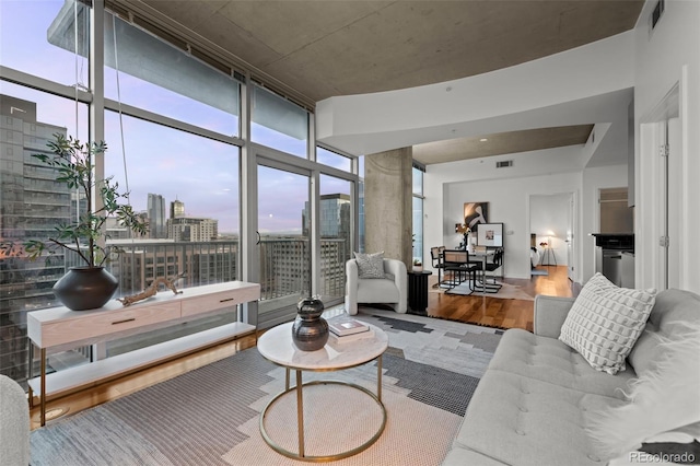 living area with a city view, floor to ceiling windows, visible vents, and wood finished floors